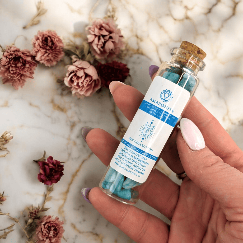 Hand holding a small glass bottle with amazonite crystal chips on a marble surface with flowers.