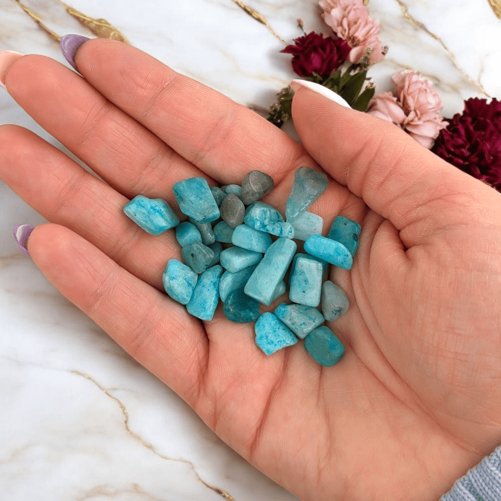 Hand holding amazonite stones on a marble surface with flowers in the background