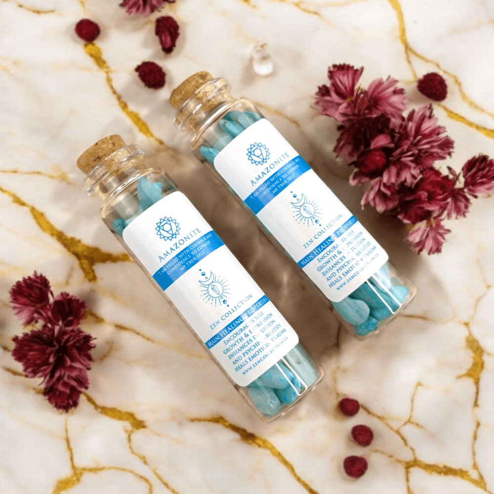 Two small glass jars containing amazonite crystals with cork lids on a marble surface with flowers.