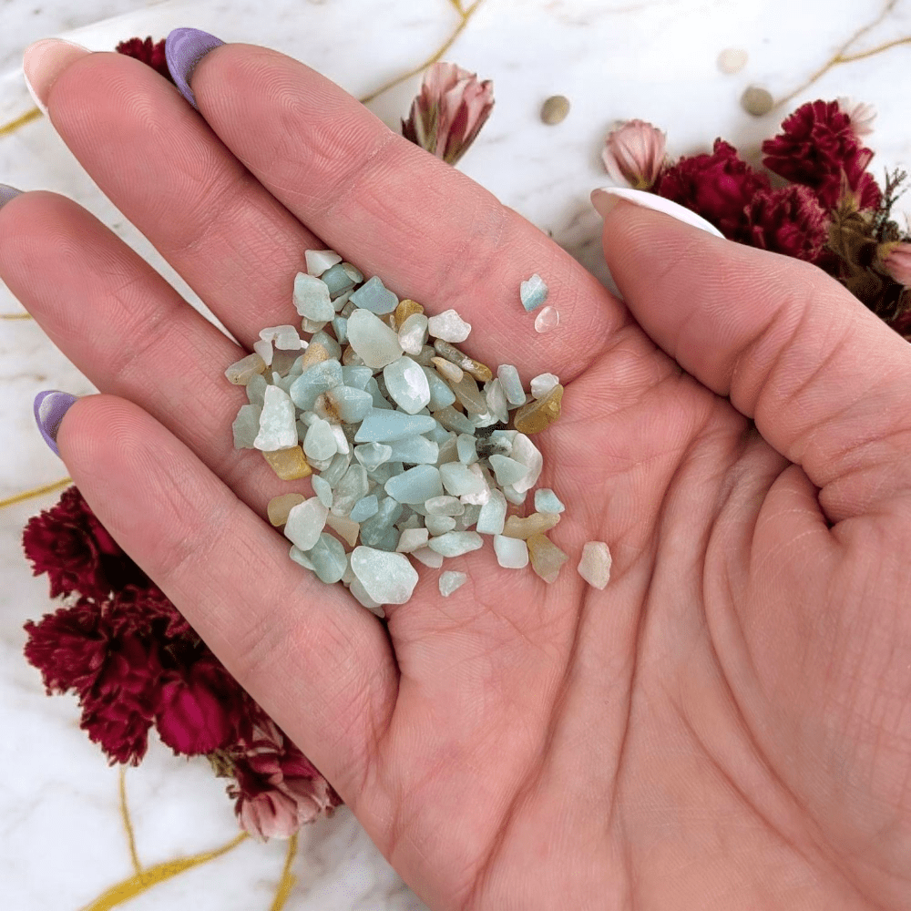 Hand holding small amazonite throat chakra stones with a floral background