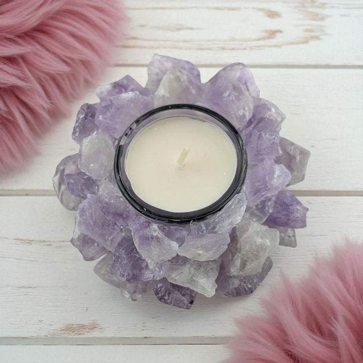 Candle in a holder made of raw amethyst crystals on a wooden surface with pink fluffy objects.