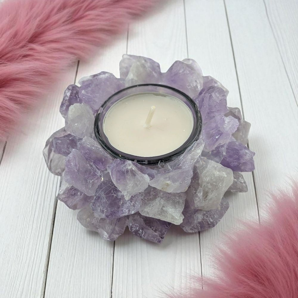 Candle holder made of purple amethyst crystals with a white candle on a wooden surface with pink fur accents.