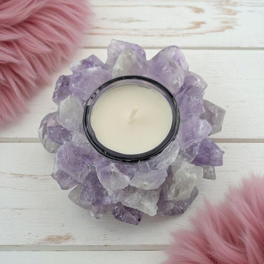 Candle in a holder made of raw amethyst crystals on a wooden surface with pink fluffy objects.