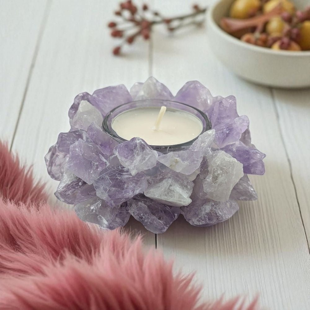 Candle holder made of raw purple amethyst crystals with a candle inside on a light wooden surface.