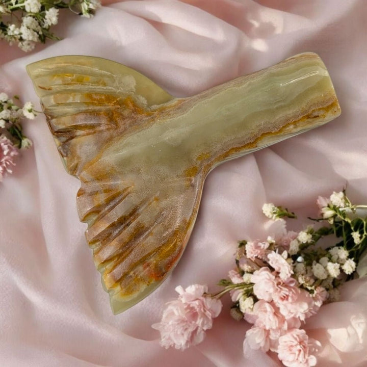 green calcite with a mermaid tail design on a soft pink fabric background with flowers.