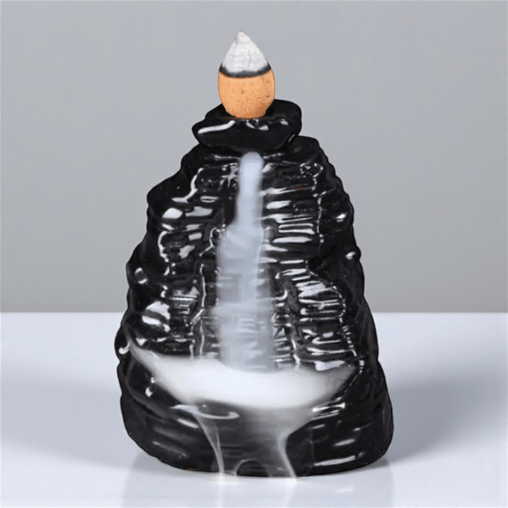 Black backflow mountain-shaped incense burner with a white smoke effect on a gray background. Shop with Zen Collection crystal store in Barrie in-store or online now.