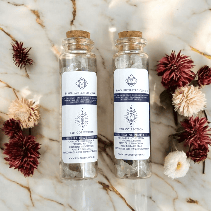 Two glass bottles filled with Black Rutilated Quartz crystals cork lids on a marble surface with flowers around.