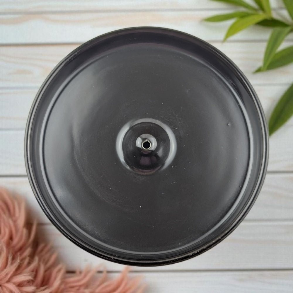 Black ceramic burner on light wooden surface with green leaves and pink flowers.