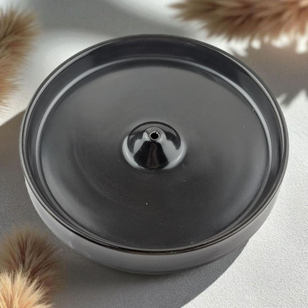 Black ceramic incense burner on a light gray surface with dried plants around