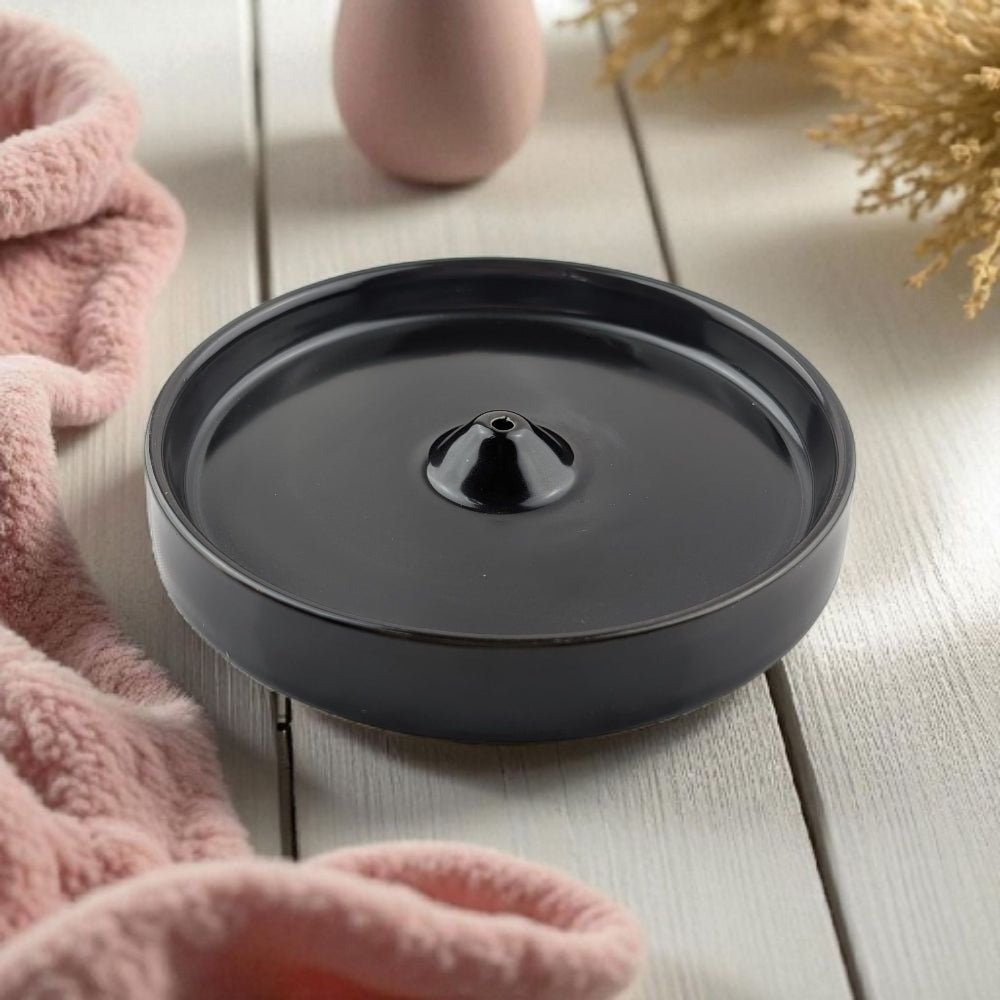 Modern Black ceramic incense burner on a wooden surface with pink towel and dried plants