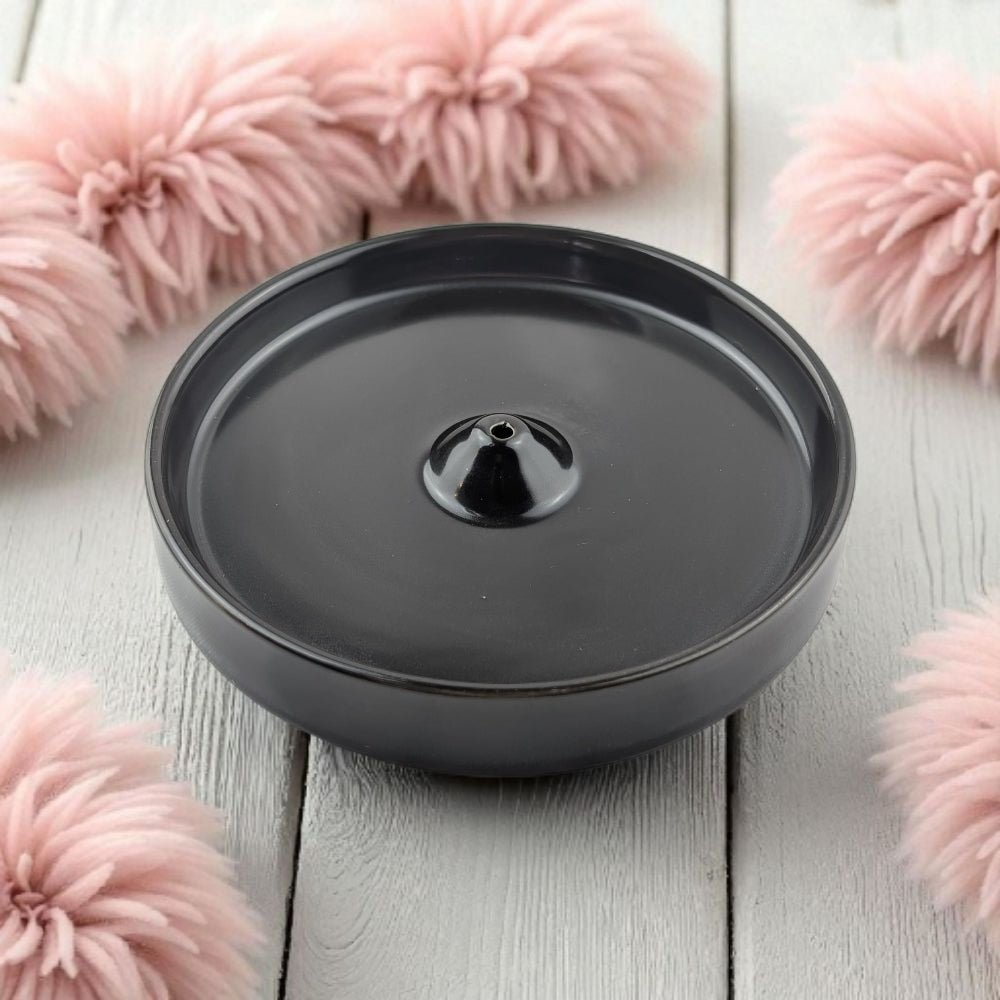 Black modern incense burner on a light wooden surface with pink floral decorations.