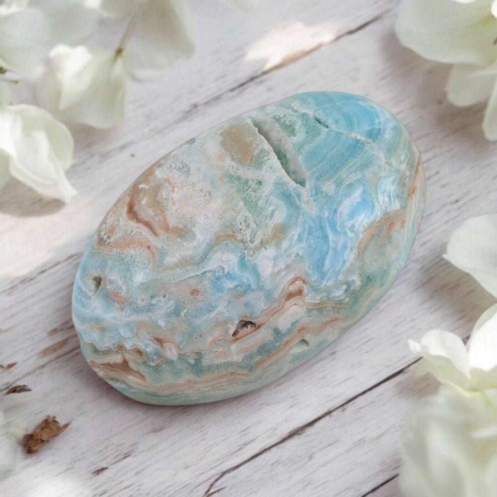Marbled Blue Aragonite palm stone for self-expression on a wooden surface with white flowers