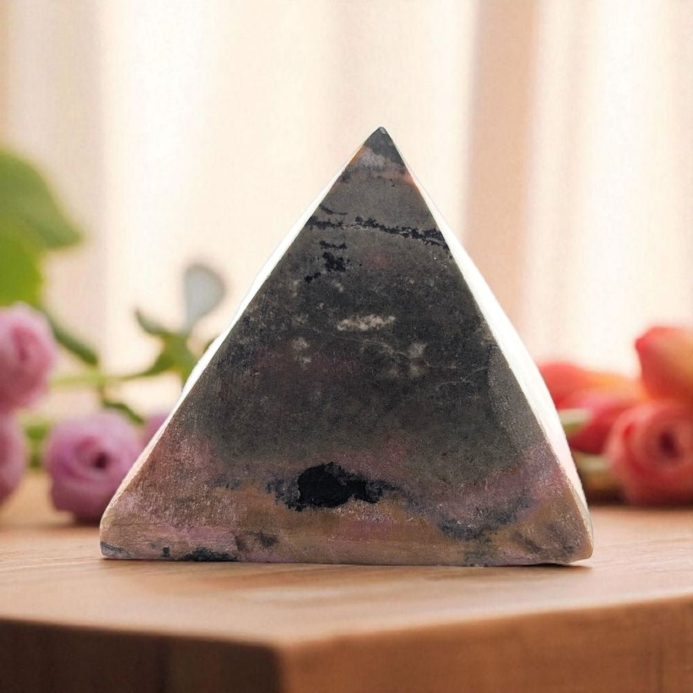 Rhodonite crystal pyramid  on a wooden surface with flowers in the background
