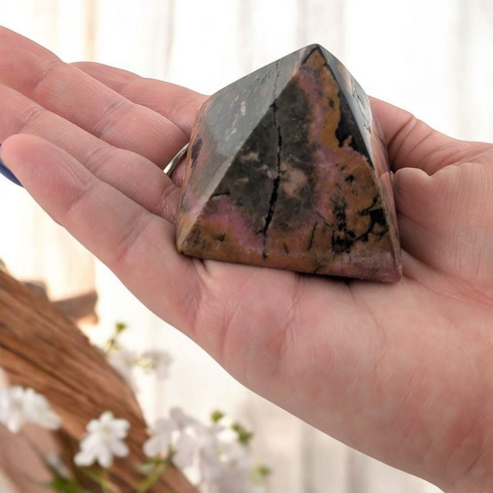 Person holding a crystal pyramid with a colorful pattern in their palm