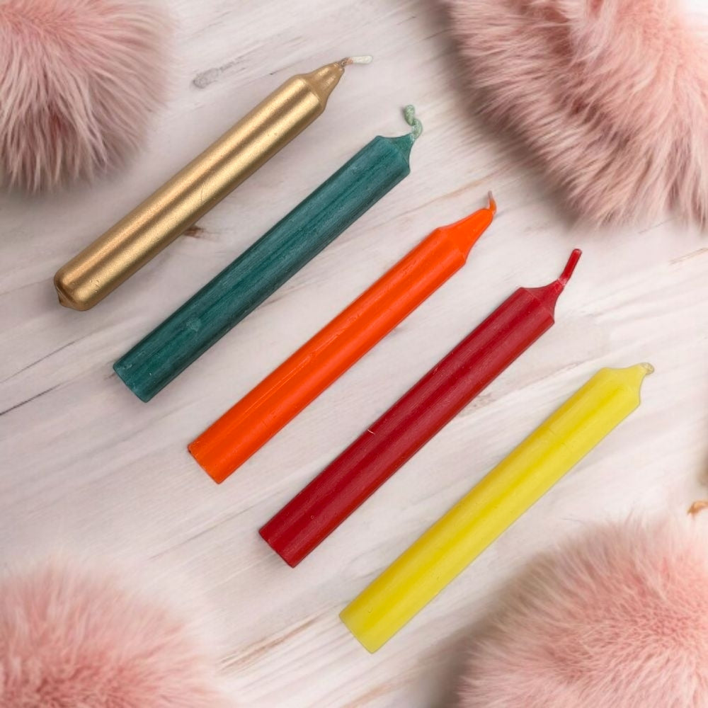 Five colorful ritual candles for steady success and humble leadership on a light wooden surface with pink fluffy objects around.