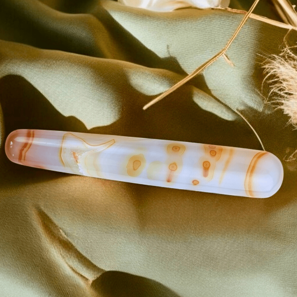 Smooth orange carnelian wand placed on a soft background.