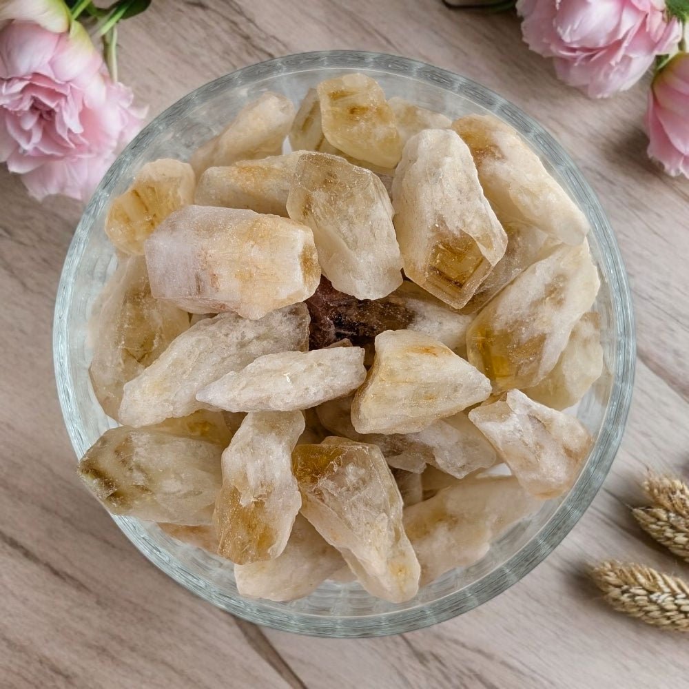 Glass bowl filled with citrine crystal points on a wooden surface with pink flowers in the background