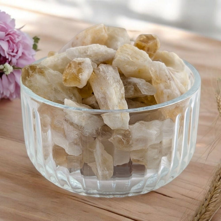 Clear glass bowl filled with heat treat citrine stones on a wooden surface with pink flowers.