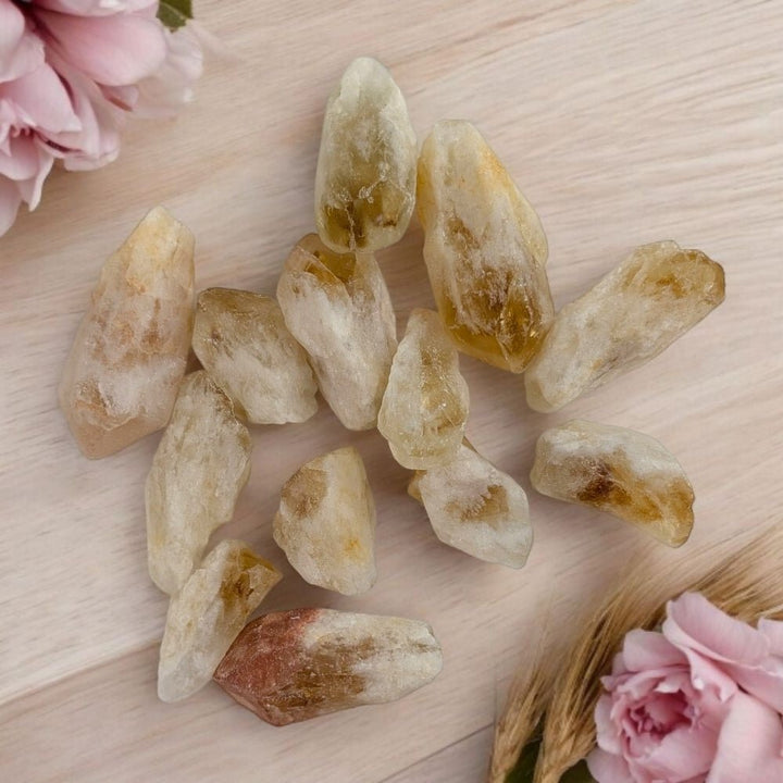 Raw citrine stones on a wooden surface with pink flowers