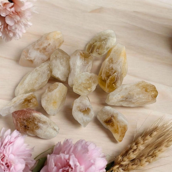citrine points on a wooden surface with pink flowers and a wheat stalk.