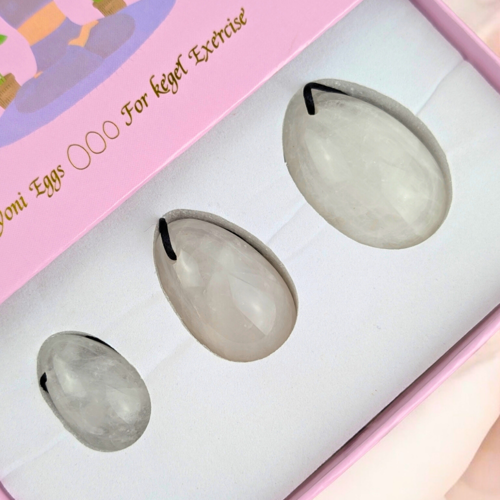 Clear quartz yoni egg set on a soft fabric background.