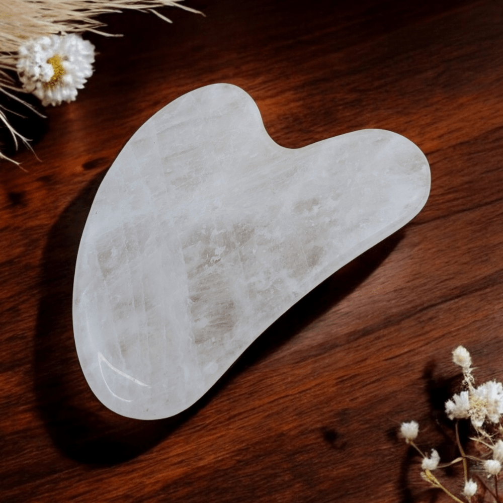 Clear quartz gua sha tool on a smooth wooden surface.