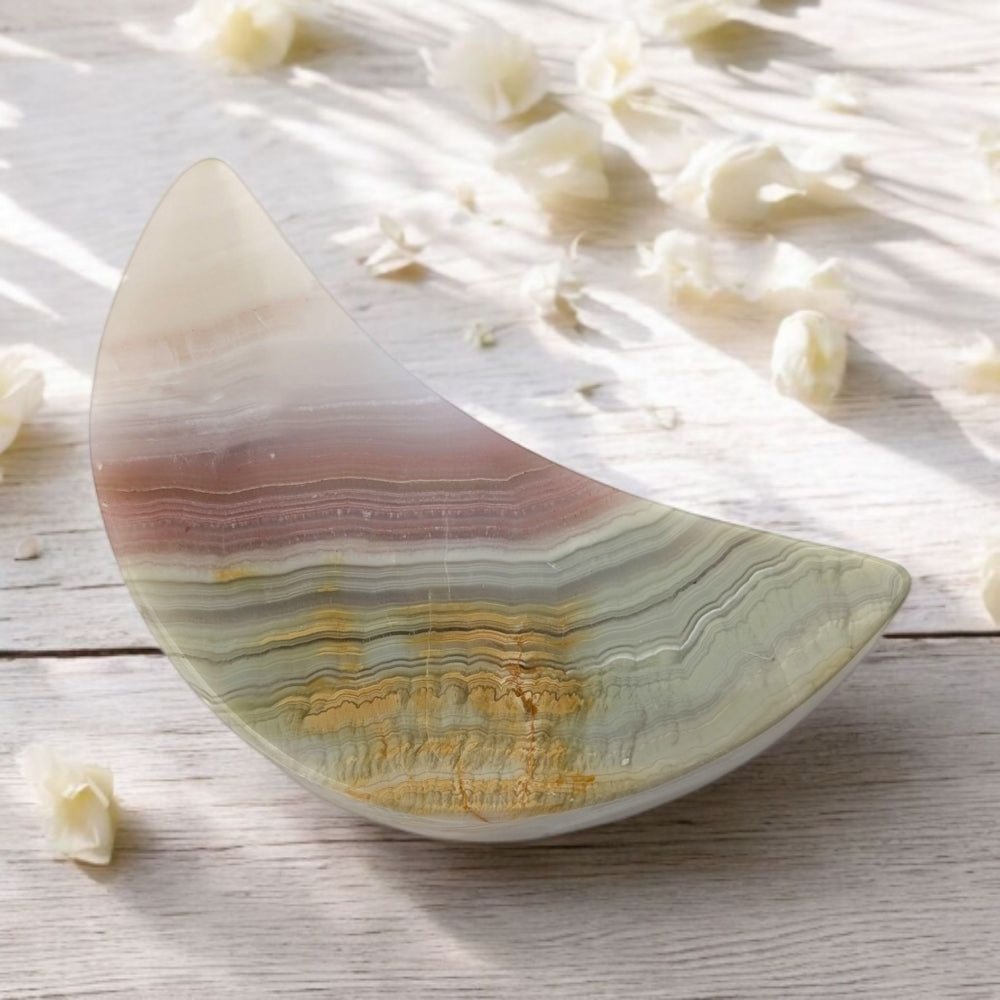 Polished crystal moon carving with multicolored layers on a light wooden surface