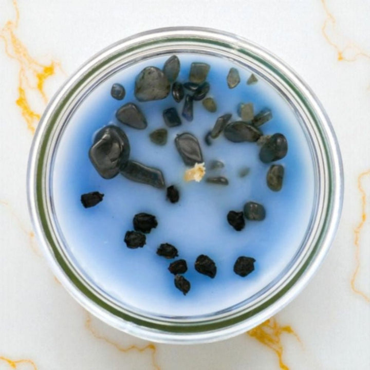 Candle Jar with blue crystals and dried  herbs on a marble surface