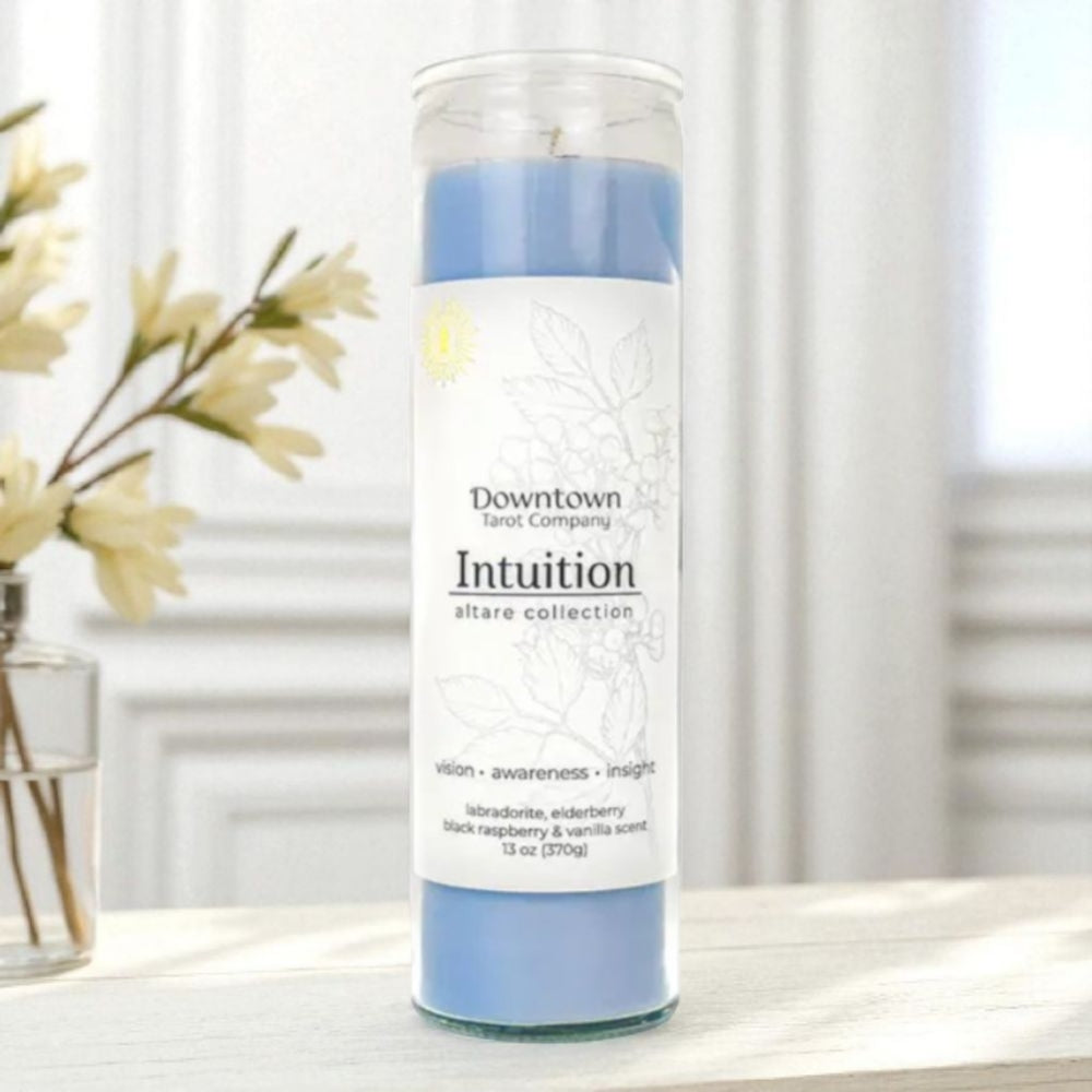 Candle with 'Intuition' label on a white surface with flowers in the background