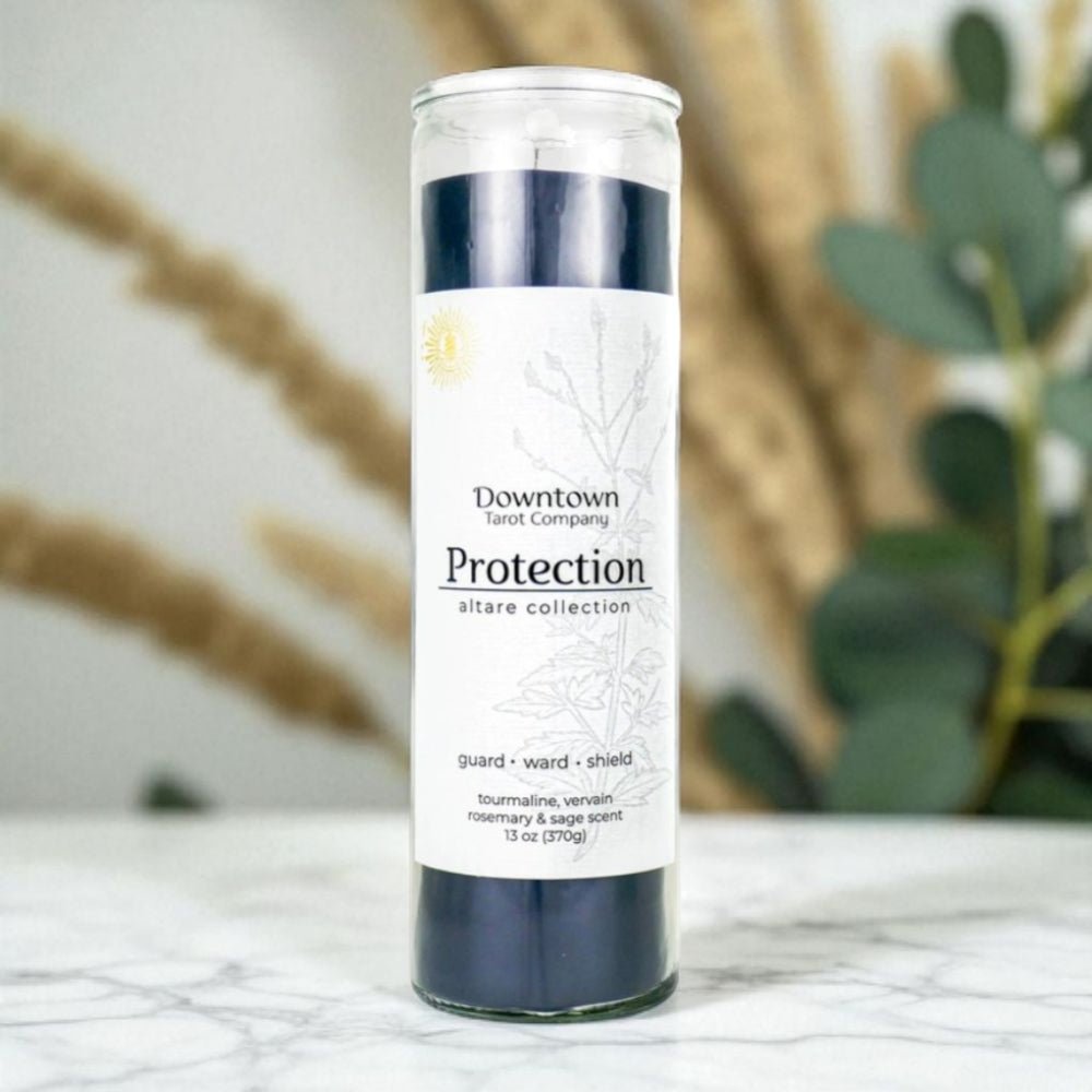 Candle with label 'Protection' on a marble surface with plants in the background.