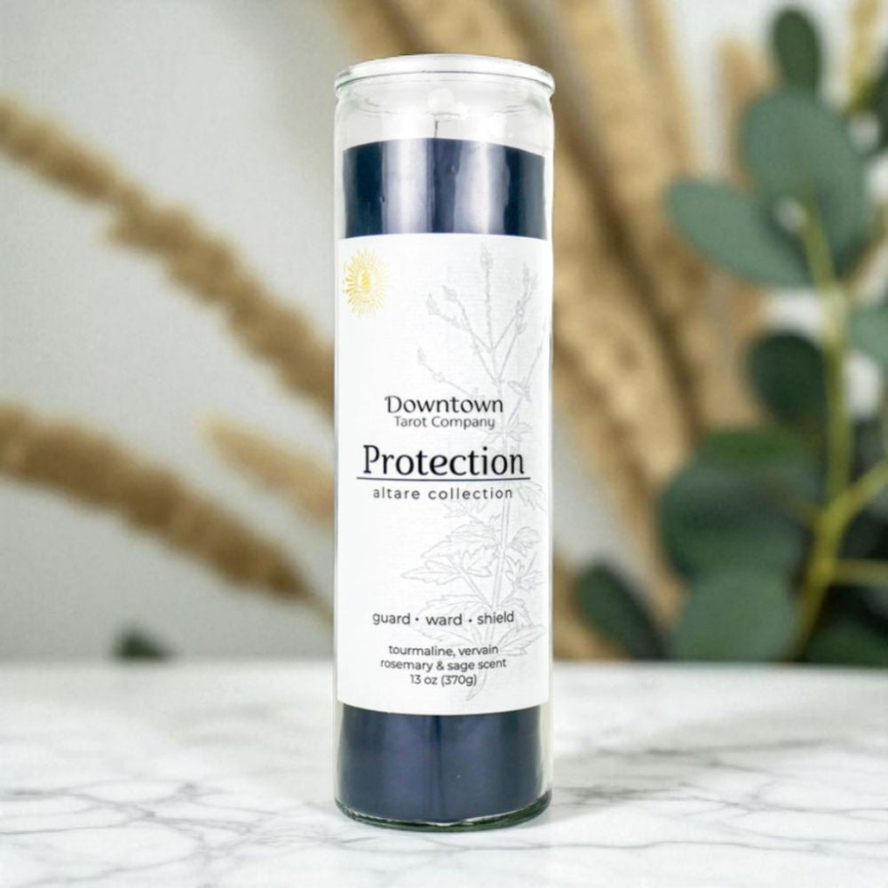 Candle with label 'Protection' on a marble surface with plants in the background.