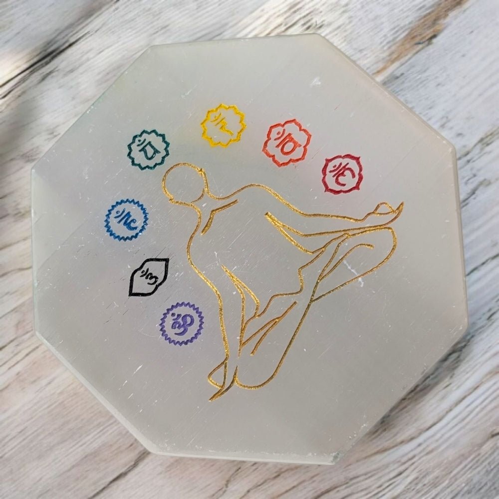 Hexagonal selenite cleansing crystal with a gold outline of a person and seven colored circles on a wooden surface