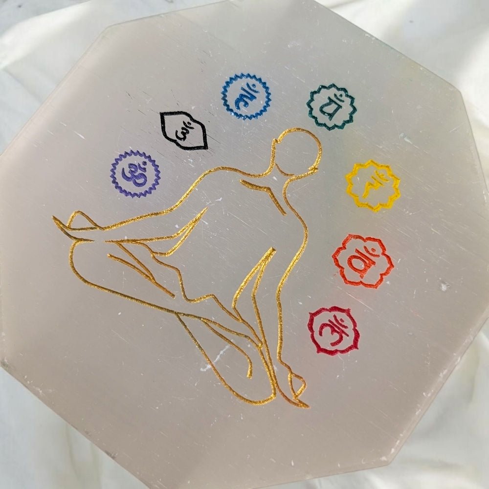 Hexagonal selenite cleansing plate with gold silhouette of a person and chakra symbols on a white background