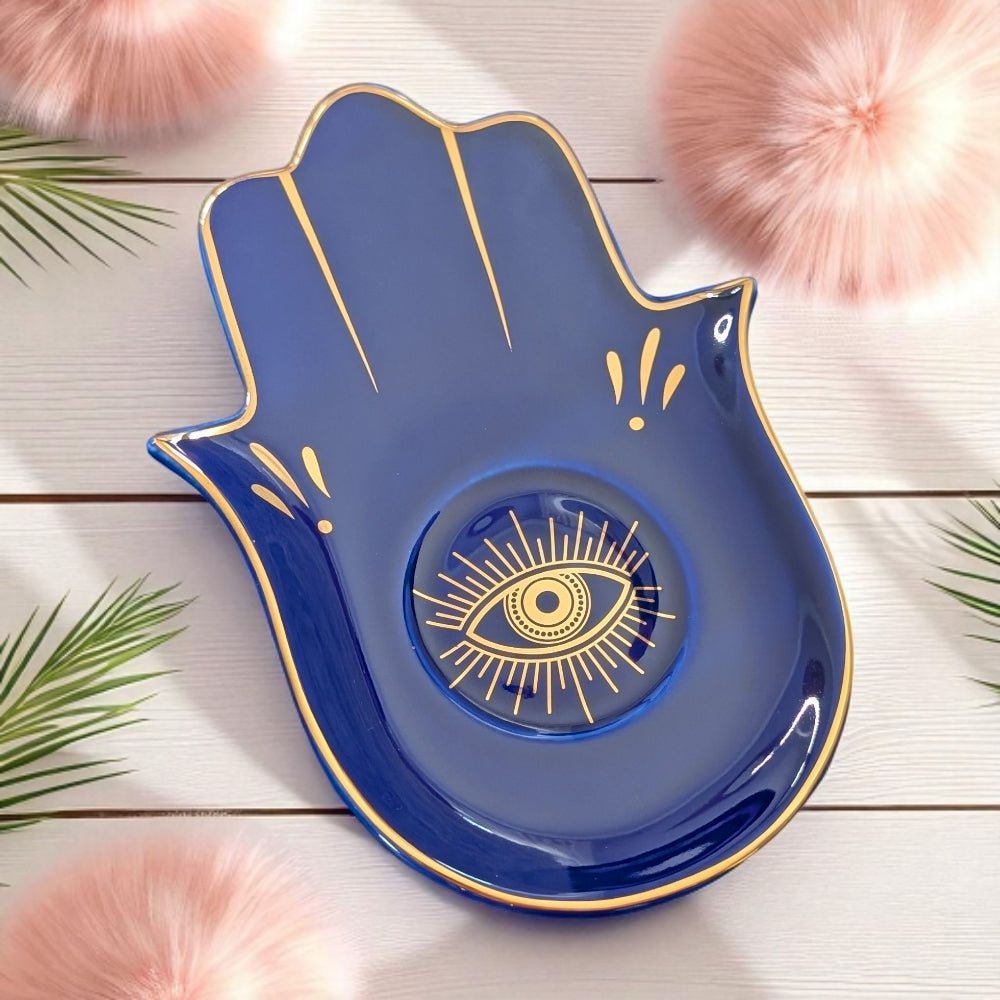Blue decorative dish shaped like a hand with a gold eye design on a wooden surface.
