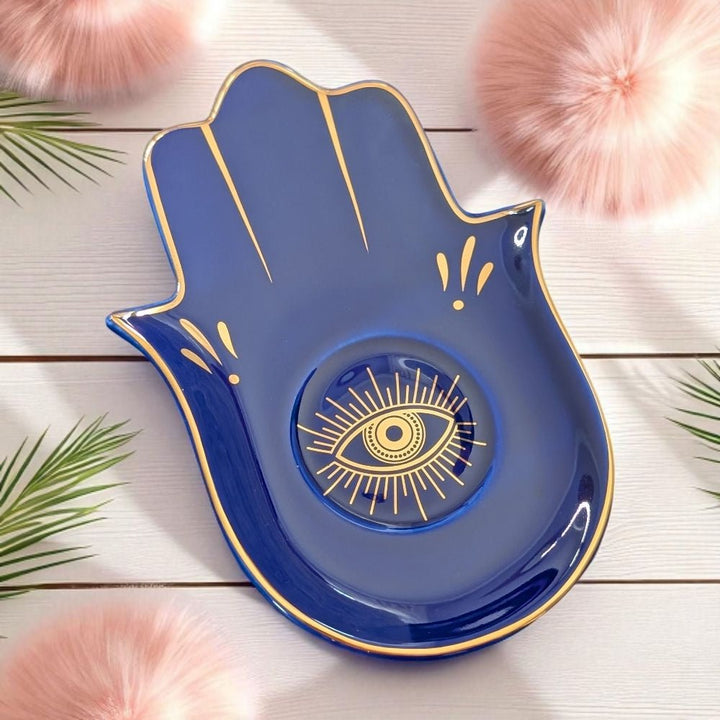 Blue decorative dish shaped like a hand with a gold eye design on a wooden surface.