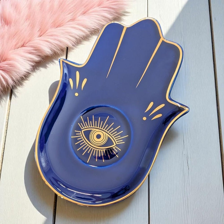 Blue ceramic dish shaped like a hand with an eye design on a light wooden surface.