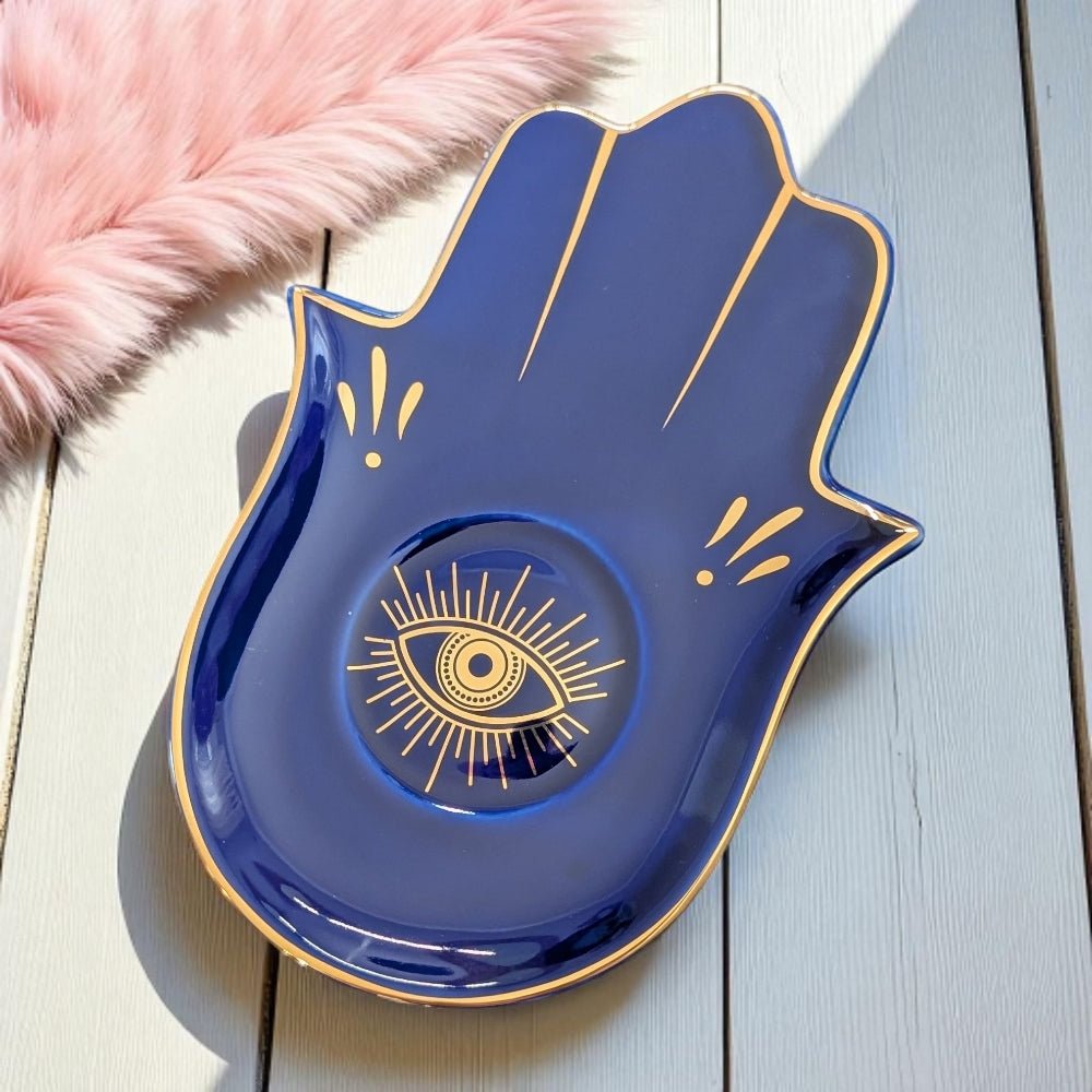 Blue ceramic dish shaped like a hand with an eye design on a light wooden surface.
