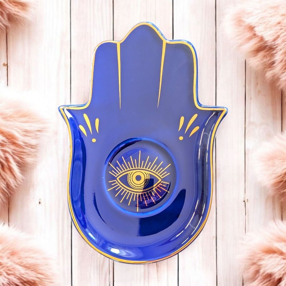 Blue Hamsa hand-shaped plate with a yellow eye design on a wooden surface.