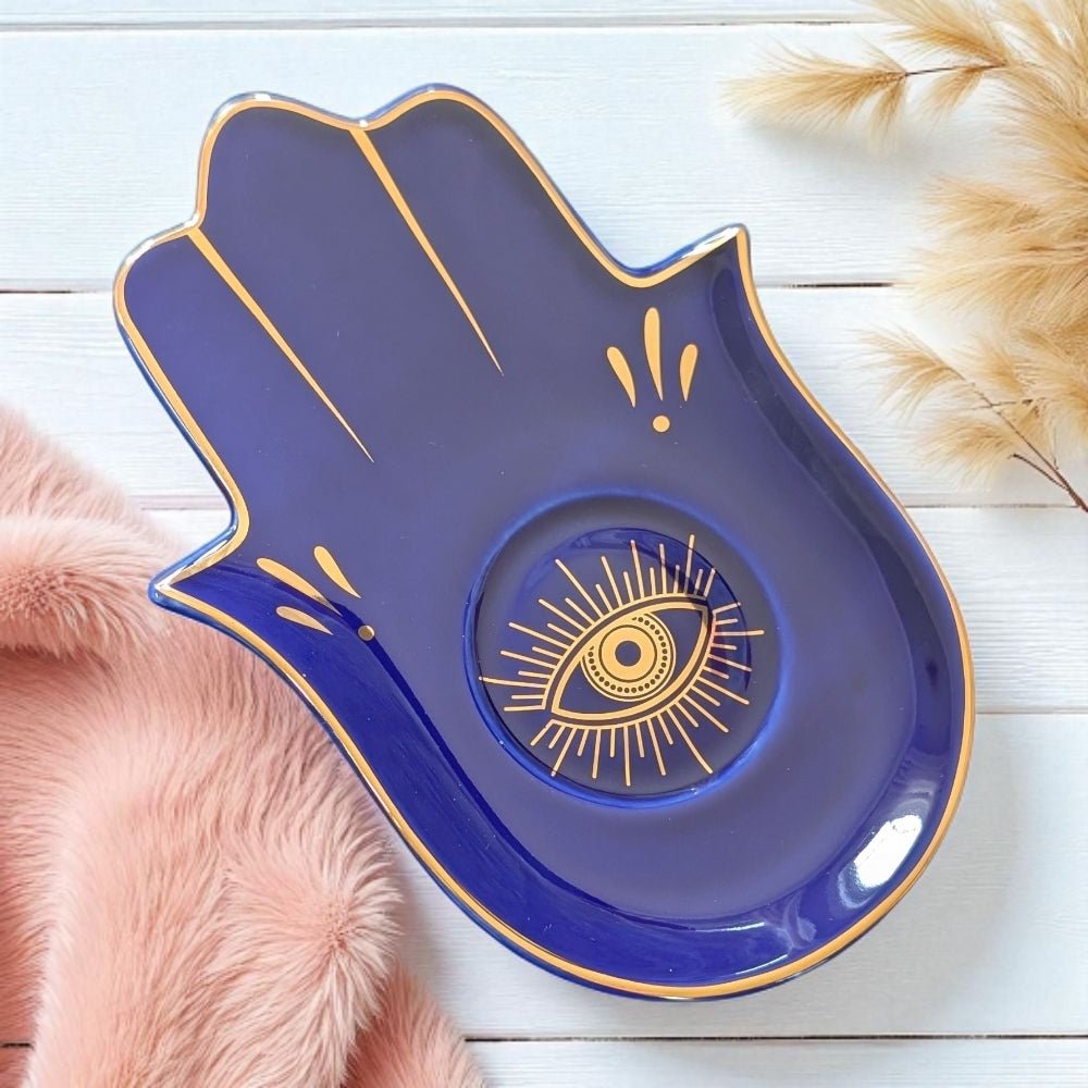 Blue Hamsa hand-shaped tray with gold eye design on a light wooden surface.