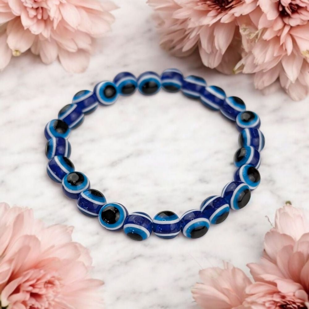 Blue and black beaded evil eye bracelet on a marble surface with pink flowers