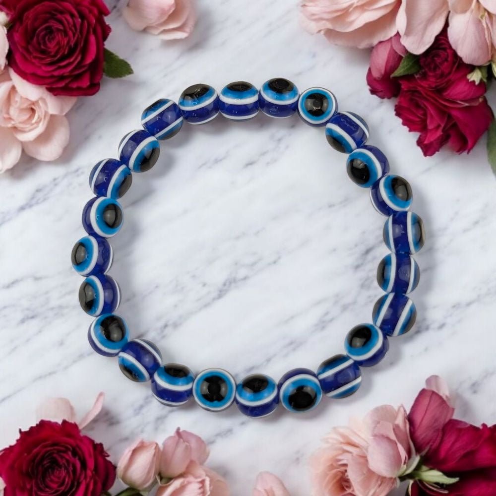 Blue and black traditional  beaded  evil eye bracelet on a marble surface with pink flowers