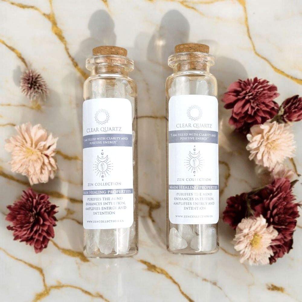 Two clear glass bottles with cork lids on a marble surface with flowers around them.