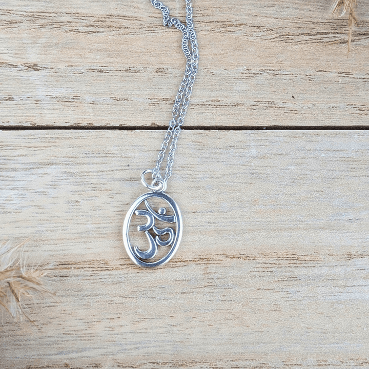 Close-up of the silver Om symbol necklace displayed on a wooden surface.