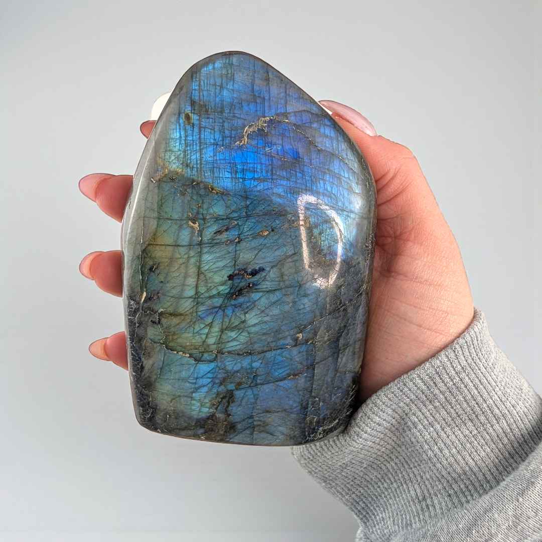 Hand holding a labradorite crystal with a blue and green pattern against a plain background
 Third eye chakra crystal available at Zen Collection Metaphysical Store in Barrie Ontario Canada. Shop In-store or Online Now 