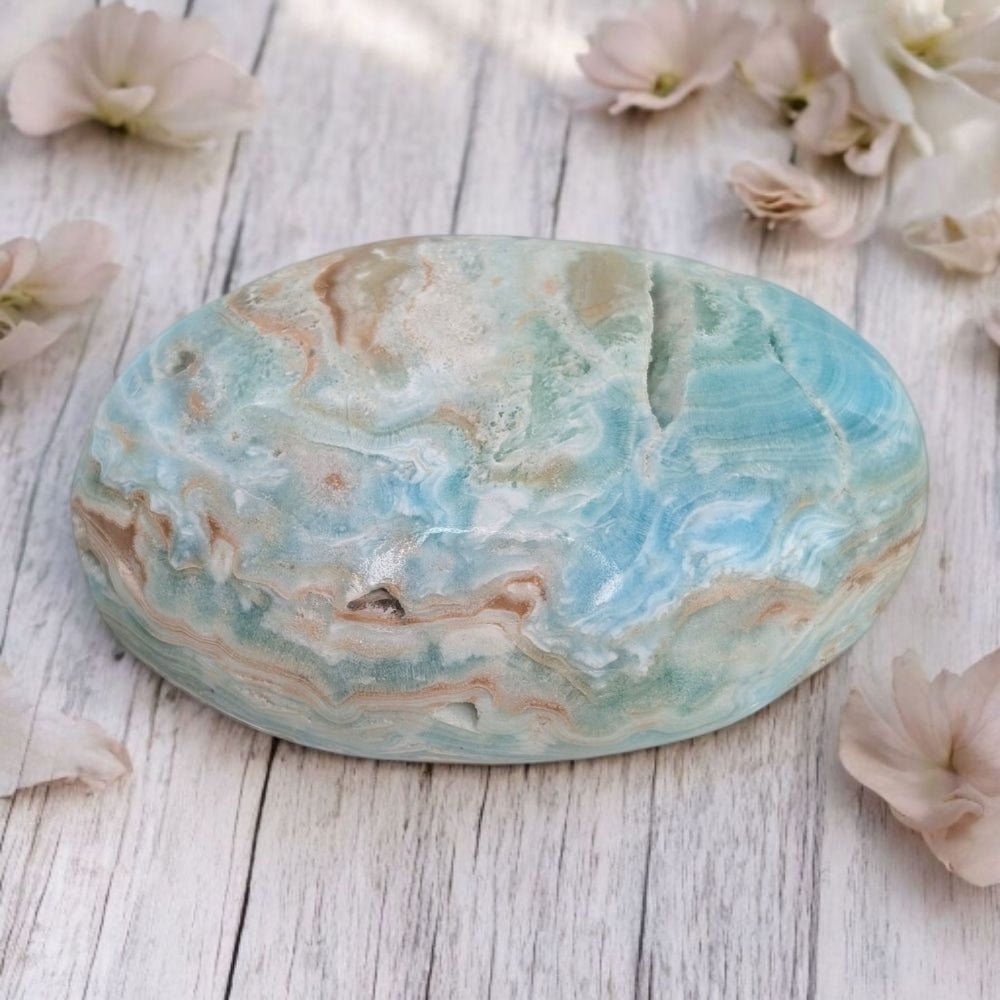 Marble-patterned Blue Aragonite crystal for emotional healing on a wooden surface with flowers around