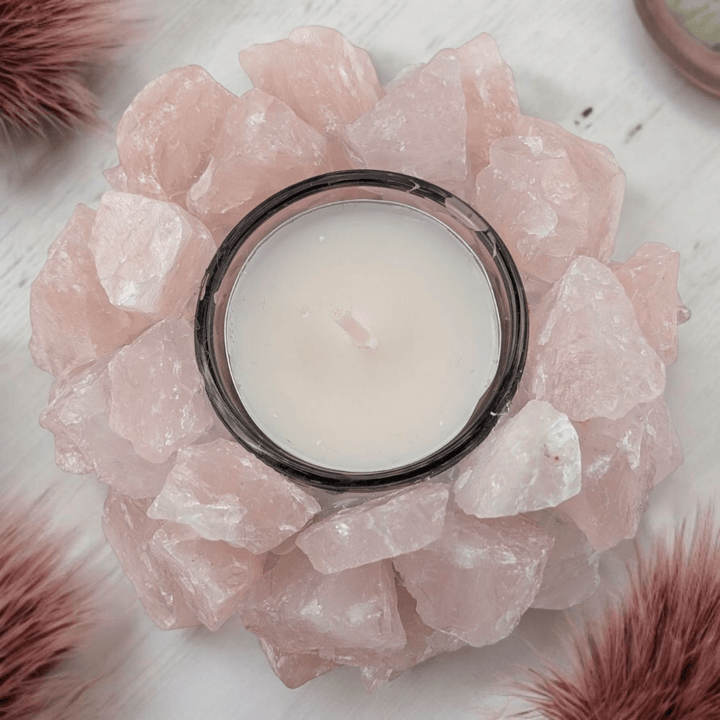 Candle in a holder surrounded by pink rose quartz crystals on a white surface.
