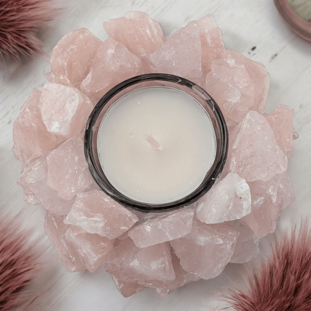 Candle in a holder surrounded by pink rose quartz crystals on a white surface.