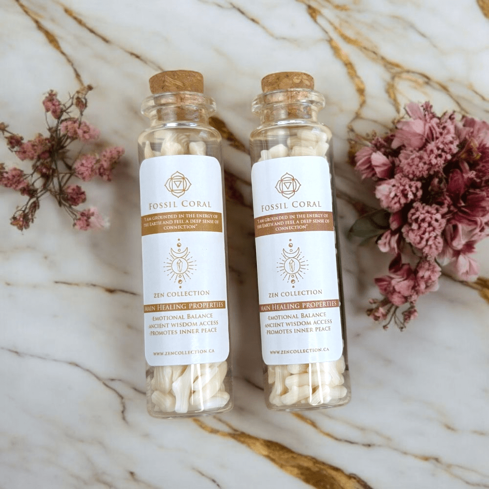Two glass bottles containing agatized coral with cork lids on a marble surface with pink flowers.