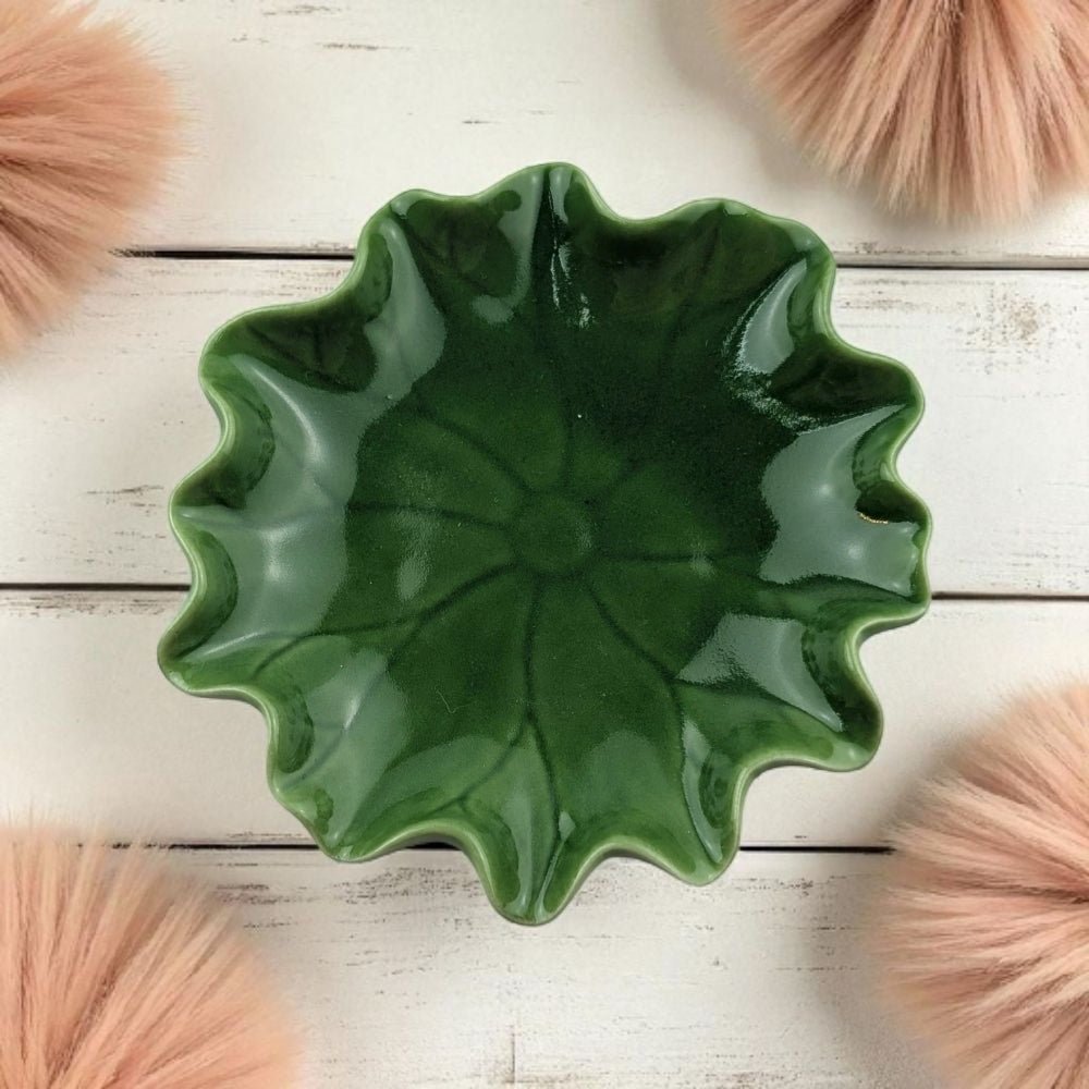 Green ceramic dish on a wooden surface with pink decorative items.
