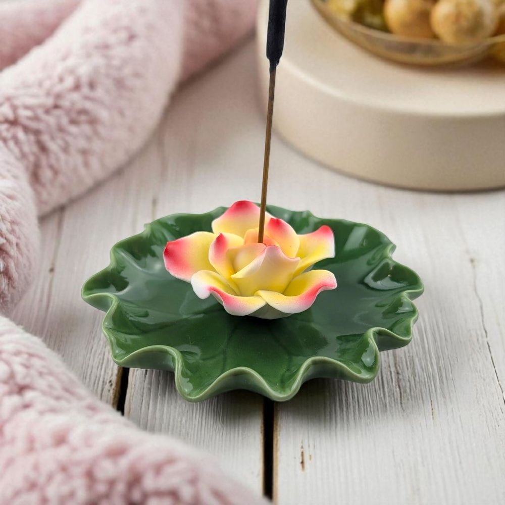 Ceramic incense holder shaped like a lotus flower with a pink and yellow petal design on a wooden surface.
